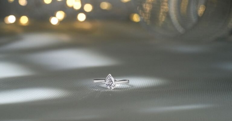 A solitaire engagement ring with a pear-shaped stone photographed with soft, warm bokeh lighting.