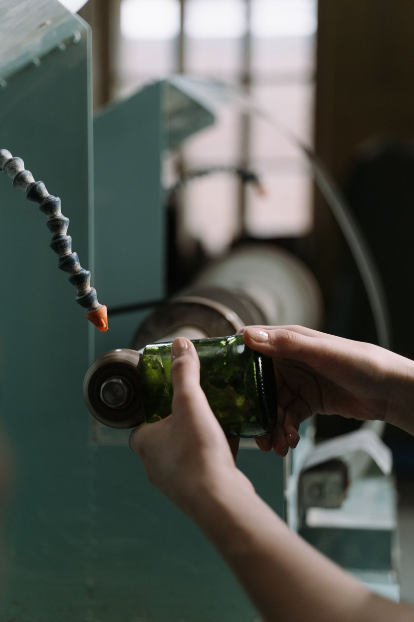 Hands holding a piece of colored glass against a spinning grinder wheel, with a water-feed nozzle dripping onto the setup.