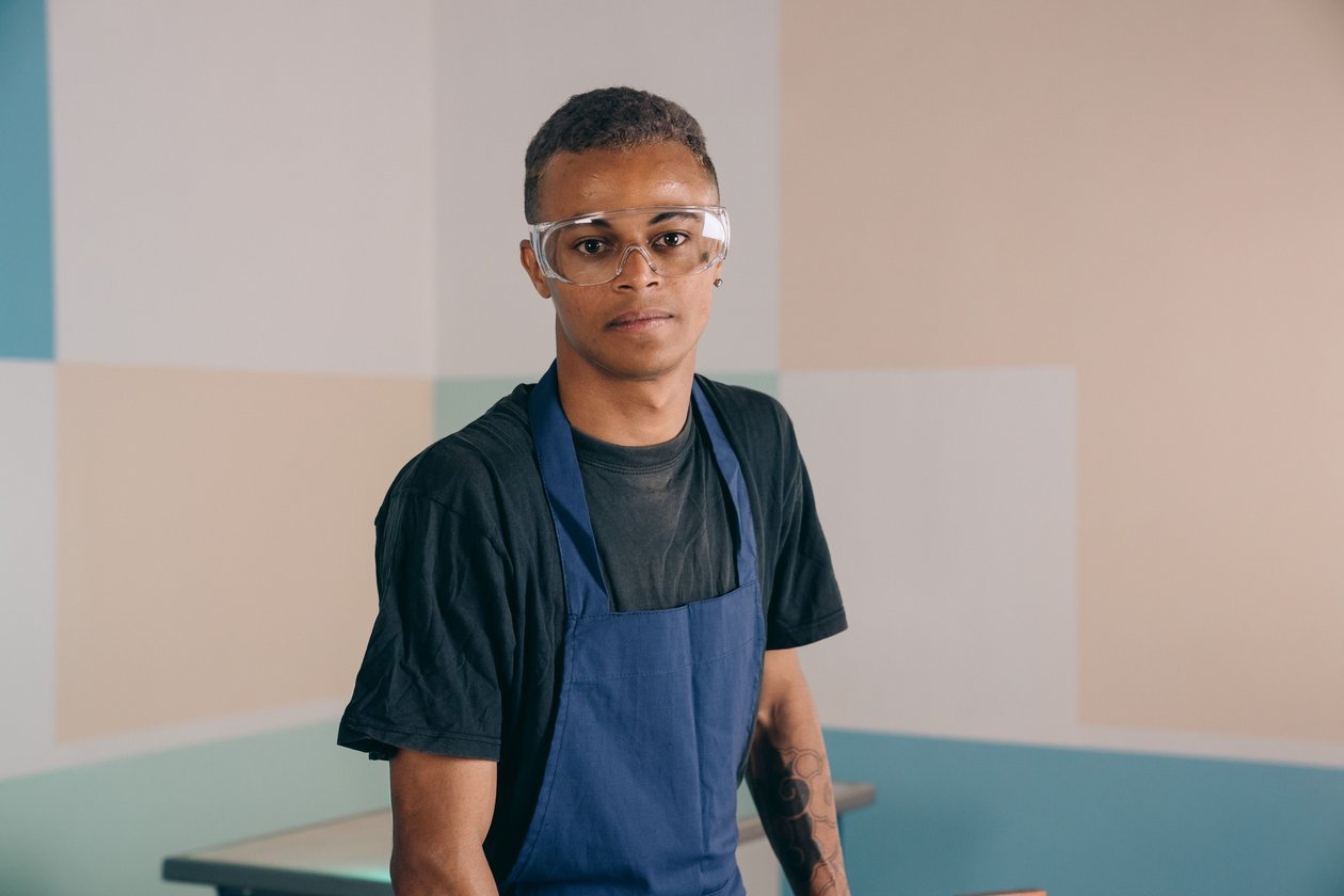 Worker wearing safety glasses and a workshop apron, representing basic personal protective equipment at the grinder.